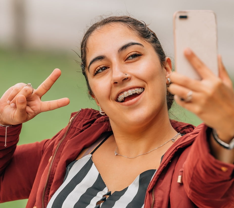 Girl with Braces Taking Selfie - Dentist in San Fernando A happy young woman with braces taking a selfie and flashing a peace sign outdoors - Dentist in San Fernando