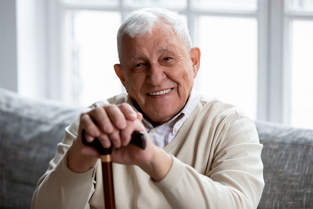 Elderly Man with Bright Smile - Dentist in San Fernando A senior man holding a cane, smiling warmly and showcasing healthy teeth - Dentist in San Fernando