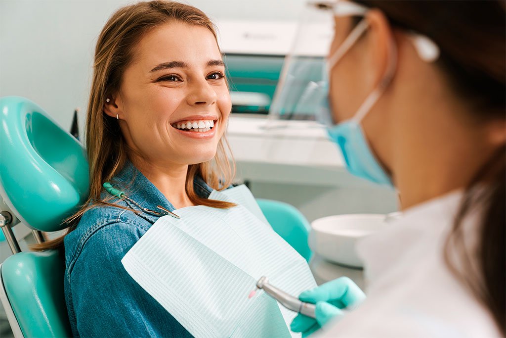 Patient Smiling at Dentist - Dentist in San Fernando A happy female patient in a dental chair smiling while a dentist prepares for treatment - Dentist in San Fernando