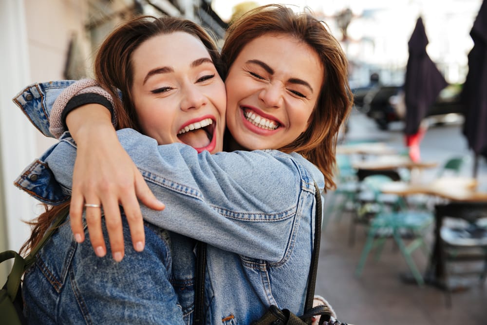 Friends Hugging and Smiling Together - Dentist in South Gate, CA Two friends share laughter and bright smiles, showcasing the happiness of strong teeth and oral health. - Dentist in South Gate, CA