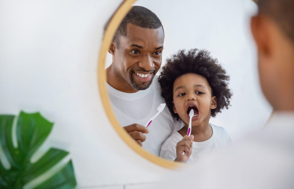 Father Teaching Child to Brush Teeth A dad and child brush their teeth together, showing the importance of building healthy dental habits early.