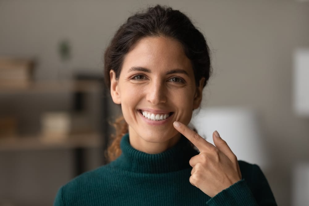 Confident Woman Showing Bright Smile - Dentist in South Gate, CA A cheerful woman points to her beautiful smile, highlighting the importance of oral health and confidence. Bright smiles start here. - Dentist in South Gate, CA