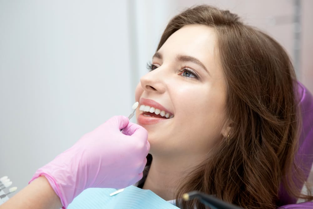 Patient Getting Veneer Shade Matched at Dentist – Veneers San Fernando CA A dental professional holds a shade guide to a patient’s teeth, ensuring a perfect color match for cosmetic veneers that blend seamlessly – Veneers San Fernando CA