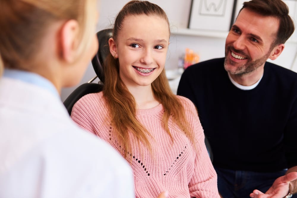 A teenage girl with braces smiles while speaking with a dental professional, accompanied by her supportive parent, highlighting a positive orthodontic visit – Dentist in Pacoima, CA.