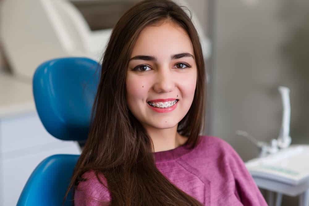A young girl with braces smiles confidently while seated in a dental chair, showcasing a positive orthodontic visit even during unexpected dental concerns – Emergency Dentist in San Fernando, CA.