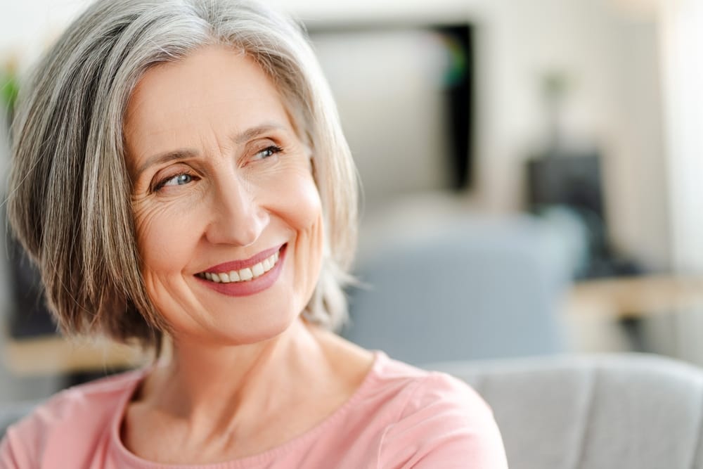 A joyful older woman with gray hair smiles warmly while looking off to the side, showcasing confidence and comfort in her healthy smile – Dentist in Pacoima, CA.