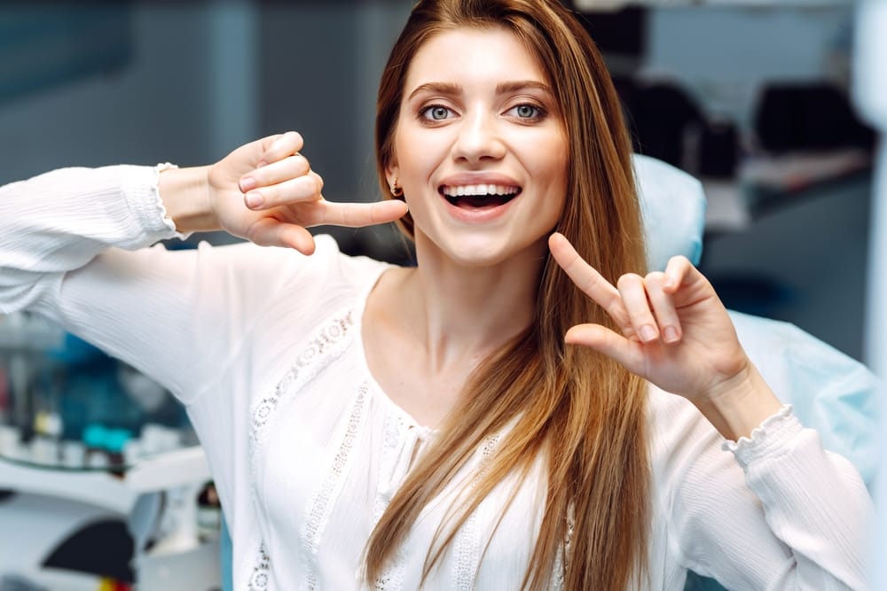 A cheerful woman sits in a dental chair pointing to her bright smile, showing confidence and satisfaction after dental care – Dentist in Sylmar, CA.